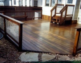 A ground-level deck built with Brazilian Walnut, a rich brown wood with multiple shades. The wood railing features a drink cap round metal balusters.