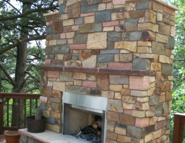 A custom stone, wood-burning fireplace on an elevated wood deck.