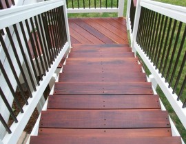 We built a staircase with 90 landing for the elevated Tiger Wood deck. The step treads, landing, and drink cap on the railing are all in Tiger Wood. The railing is white stained wood with round metal balusters in matte black.