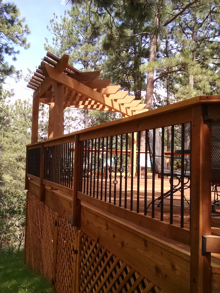Deck railing made of redwood components with round metal balusters that feature a basket design.