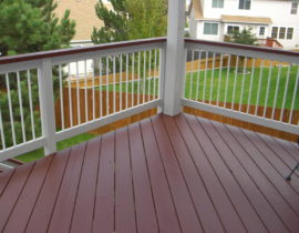 This refinished deck has two, solid body stains in contrasting colors. The decking and drink cap are in a redwood shade, while there railing is stained in white with white balusters.