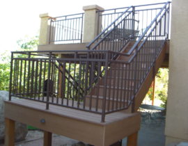 Composite deck with 3'-wide, closed step staircase with a 180-degree turn landing, step lights, and a custom metal railing in a brushed bronze color.