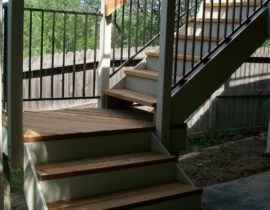 This staircase has 3'-wide, closed steps with a 90-turn landing, wood rail posts and handrail, and metal rail panels between posts.