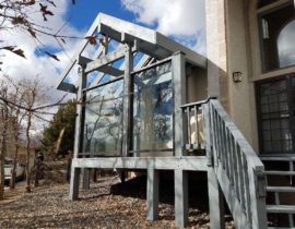 Outside view of deck with a pergola style cover and glass walls.