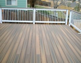 Composite deck at 90 degree angle. The railing is white composite components with white balusters and a drink cap in the same material as the decking.