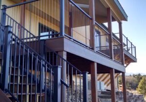 This covered deck features a unique railing. It is black metal posts with vertical, stainless steel cables. The stair rail has round metal balusters instead of cables.