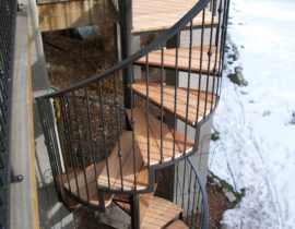An elevated deck with a spiral staircase that has a wrought iron railing. The railing has twisted balusters with a knuckle element on some of them.