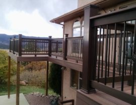 A beautiful, elevated deck featuring a double picture frame around 45-degree angle boards. The railing has composite components and drink cap with round metal balusters. Some of the balusters feature a basket design.