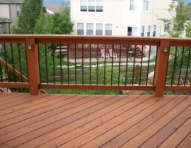 The redwood decking is laid at a 45-degree angle. The railing features redwood posts, each with a post light attached. Round metal balusters feature a basket design and there is also a redwood drink cap.