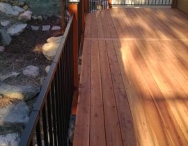A Redwood deck with 90-degree boards, black, metal panel railing with wood posts and lights on each post.