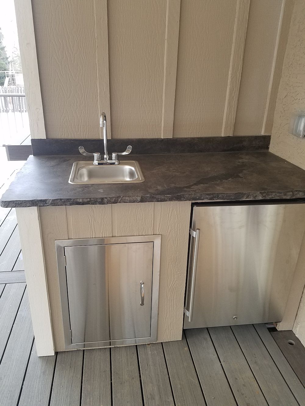 Mini outdoor kitchen with a fully-functioning sink, refrigerator, and granite countertop