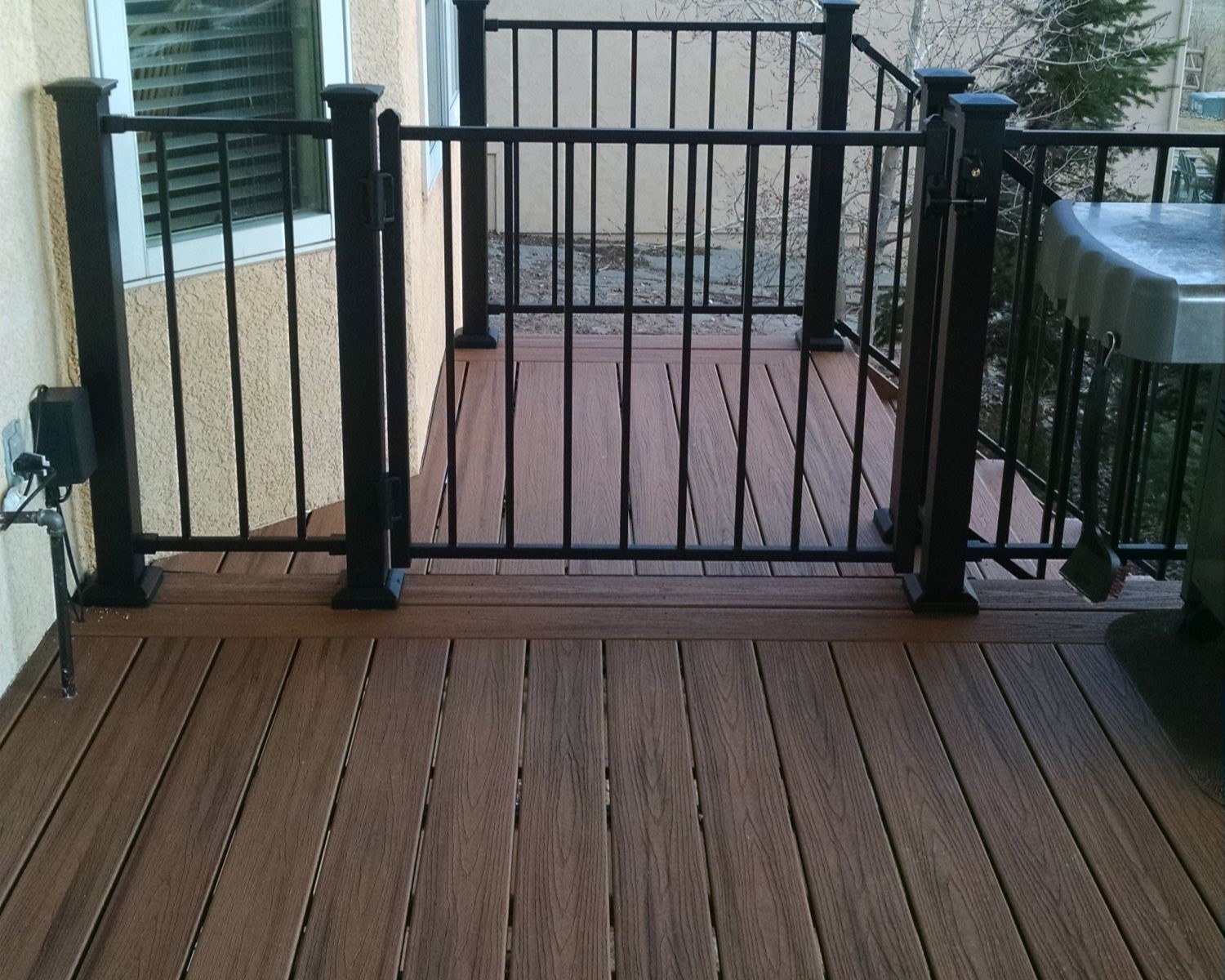 Custom deck featuring composite boards with double end and dividing boards. The railing is a metal panel system with gate installed at top of steps.