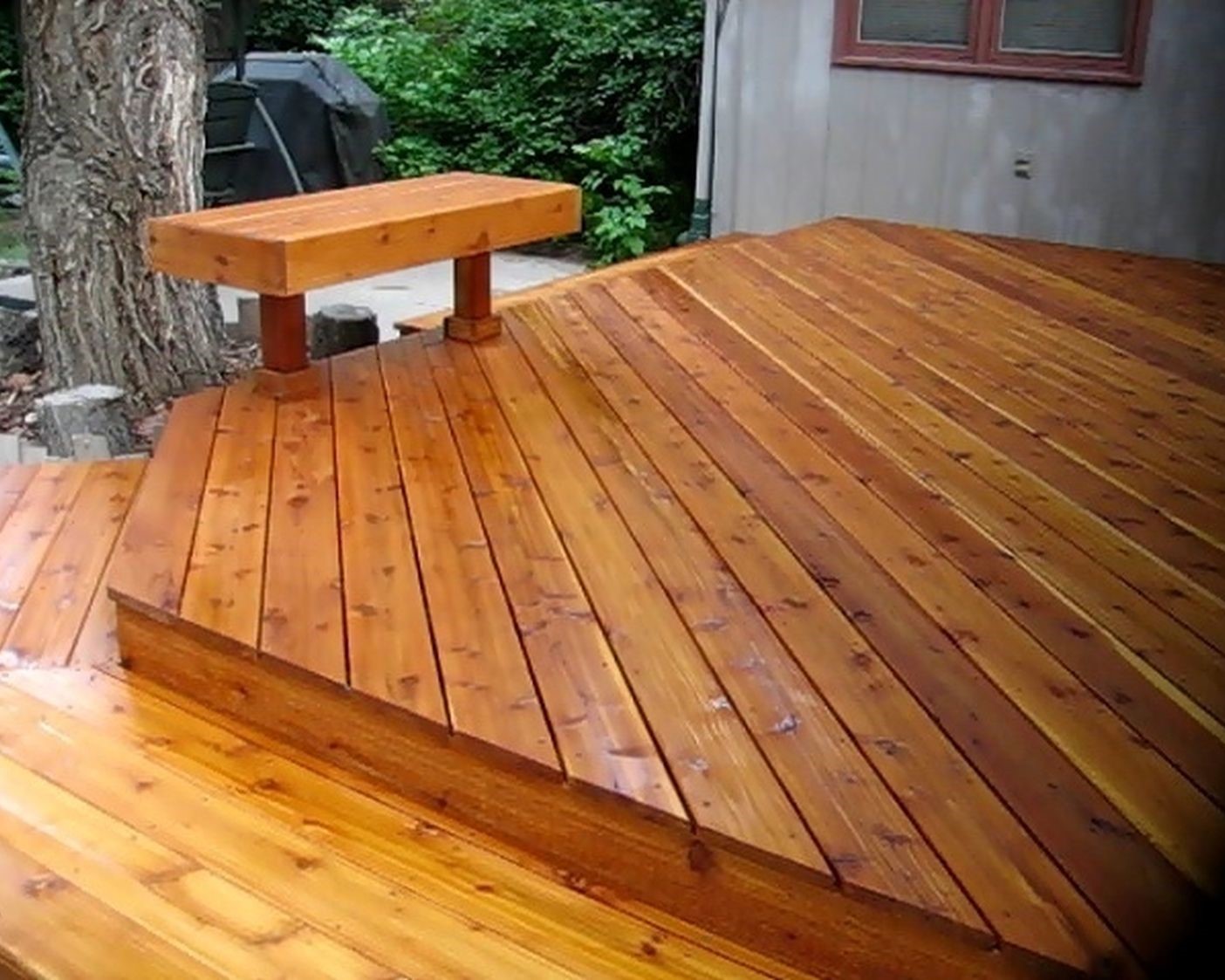 Cedar deck with the boards laid at a 45-degree angle and a single, wide step that encircles the deck.