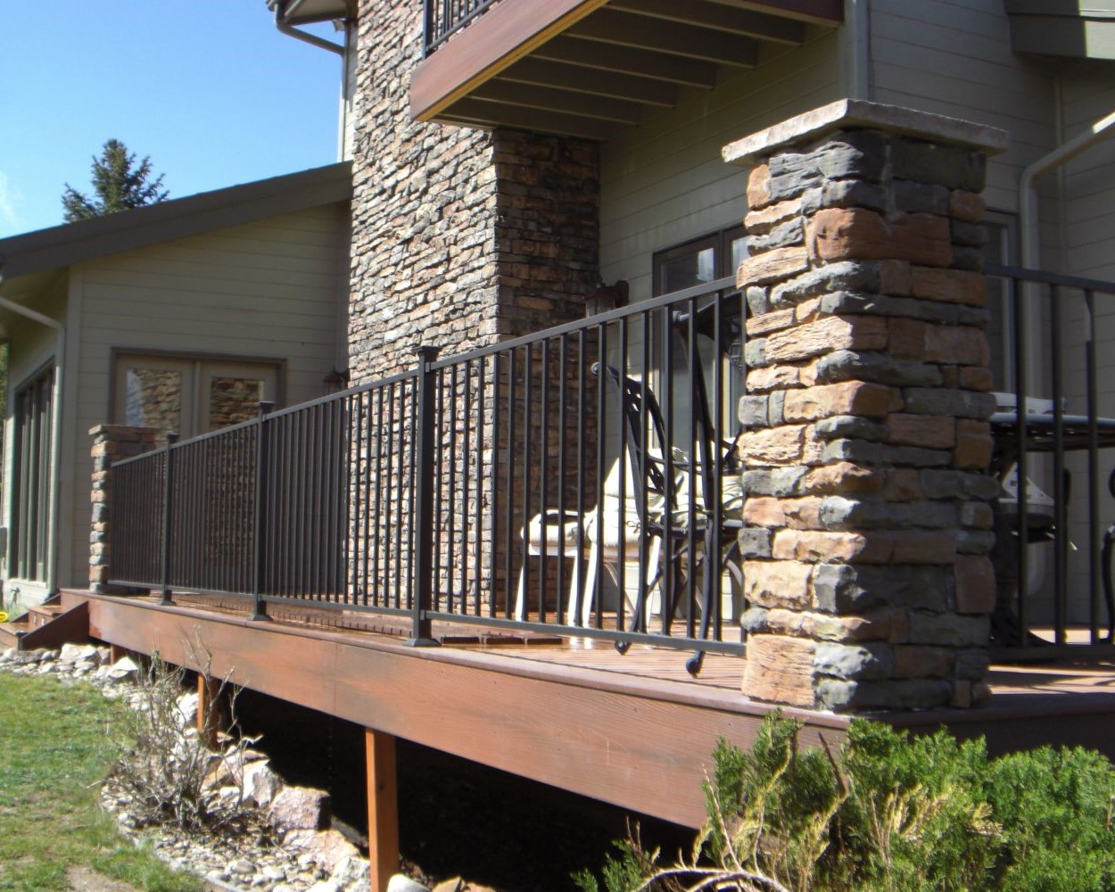 Composite deck with composite fascia installed. Black metal railing anchored by stone columns.
