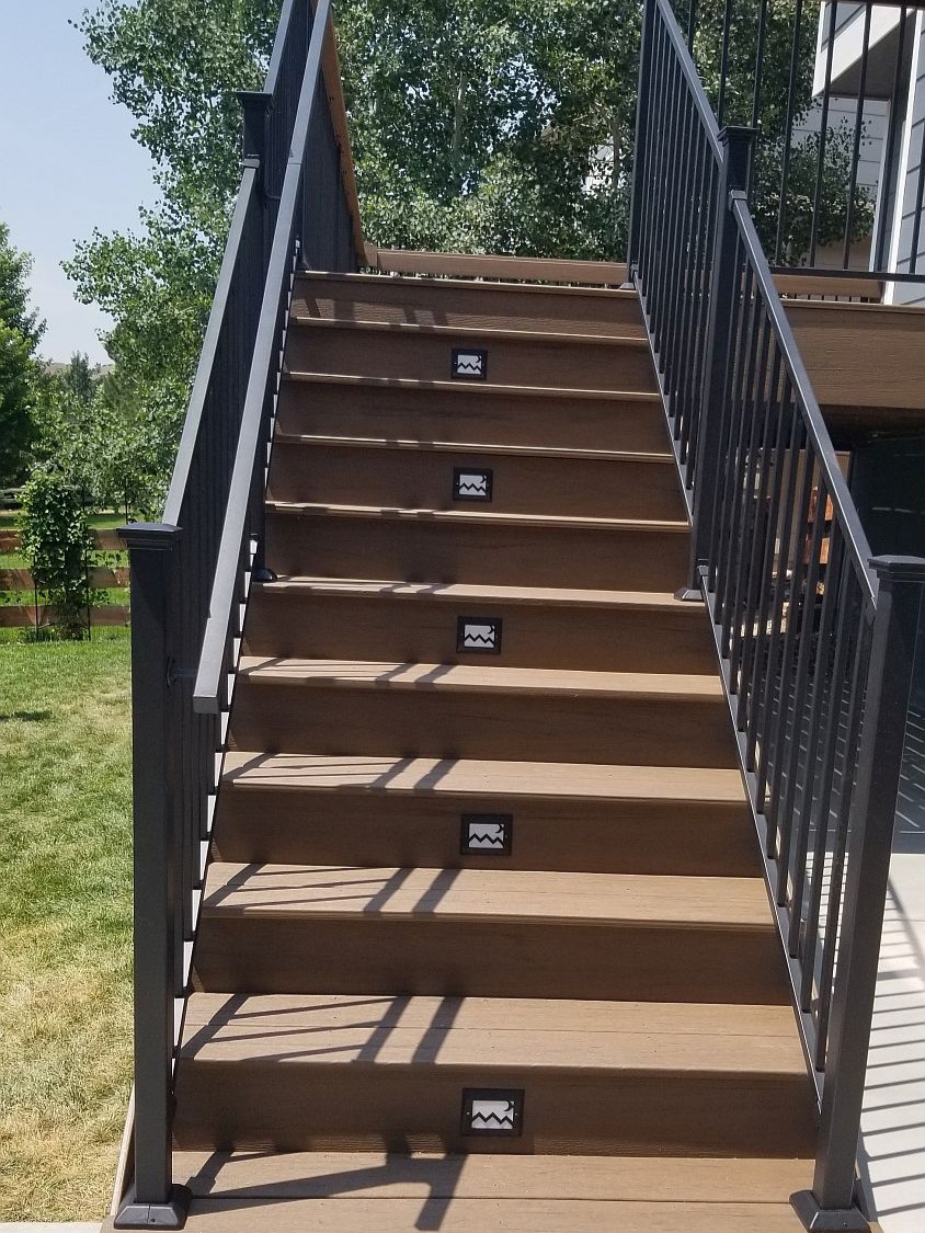 Deck staircase with composite treads and risers, metal panel railing and step lights.