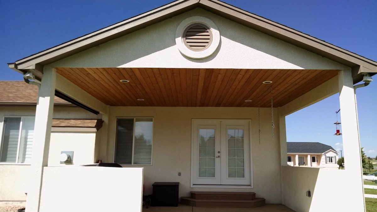 Gabled deck cover with a tongue and pine flat ceiling over a custom deck featuring a stucco gas fireplace.