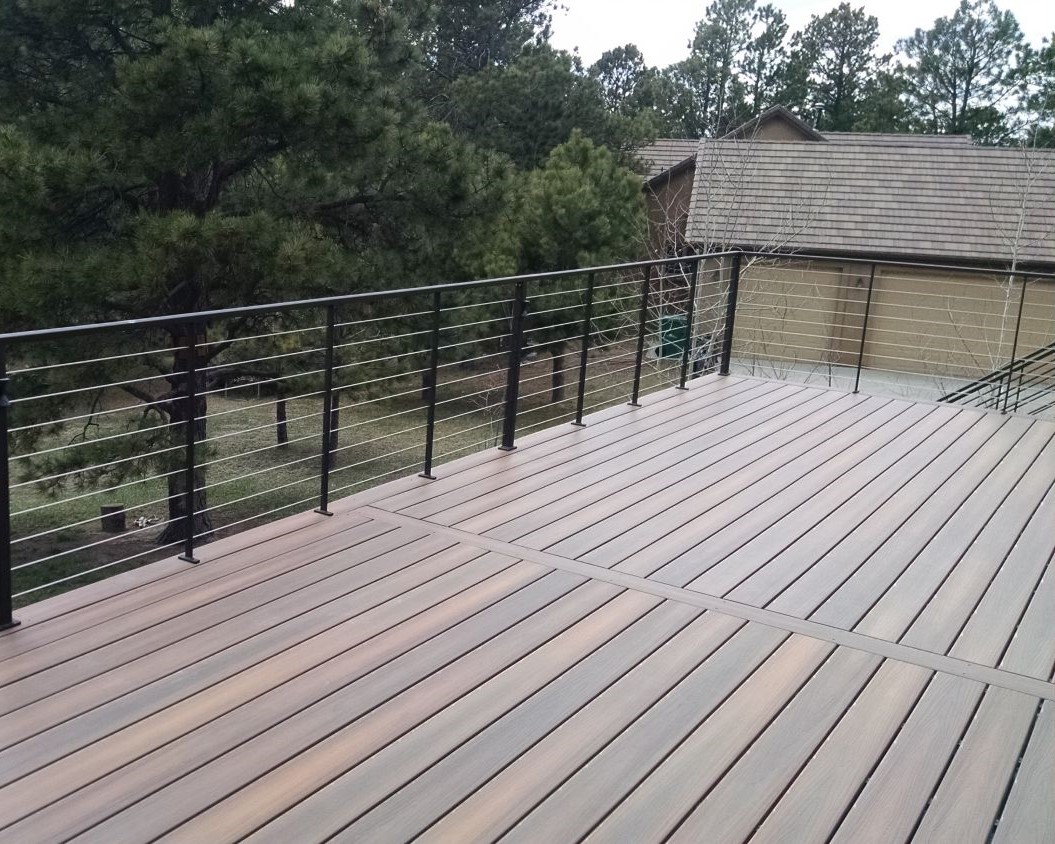 A large composite deck that has a metal railing with stainless steel horizontal cables between the posts.