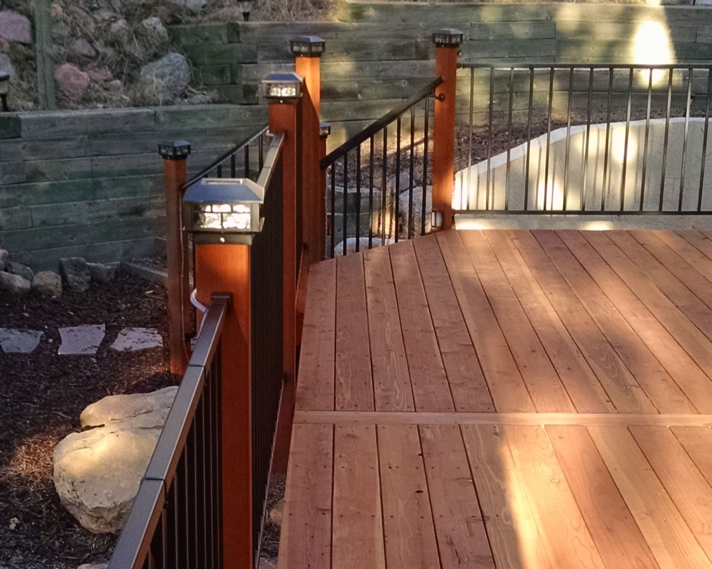 Redwood deck with a metal panel railing anchored by wood posts. Each railing post features a lighted post cap.