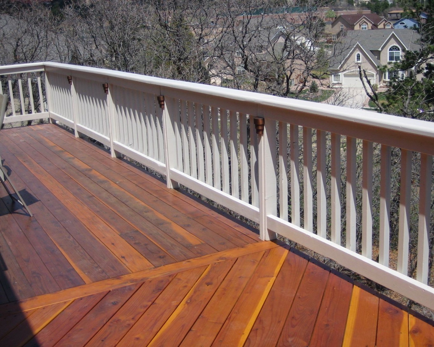 Wood deck built with the boards laid at multiple angles. The snow fence railing features a drink cap and post lights. It is is painted in white, a stark contrast to the deck's wood colored stain.