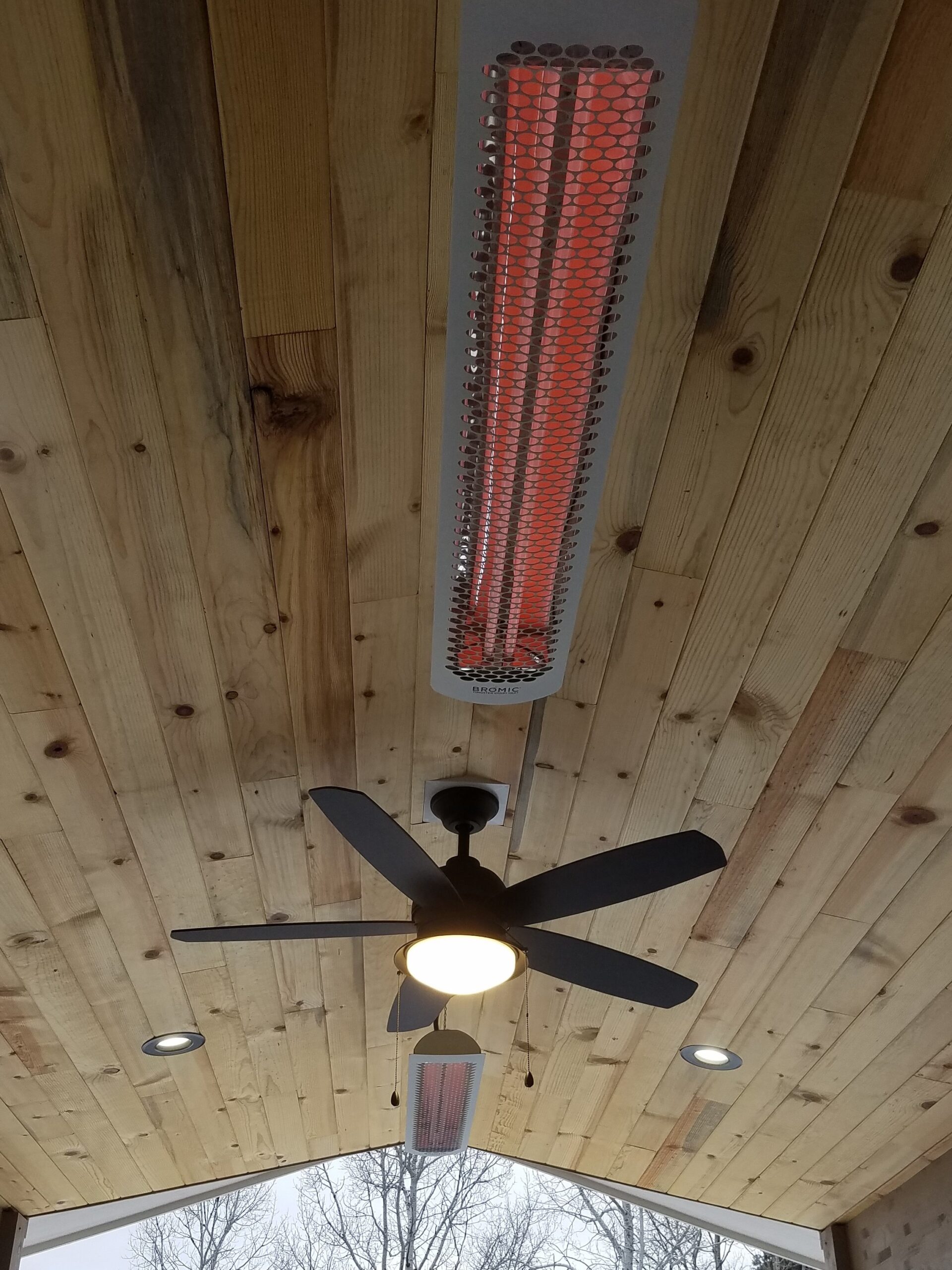 Deck cover with a vaulted ceiling in Blue Stain pine. It also includes recessed lights, a ceiling fan, and two overhead heaters.