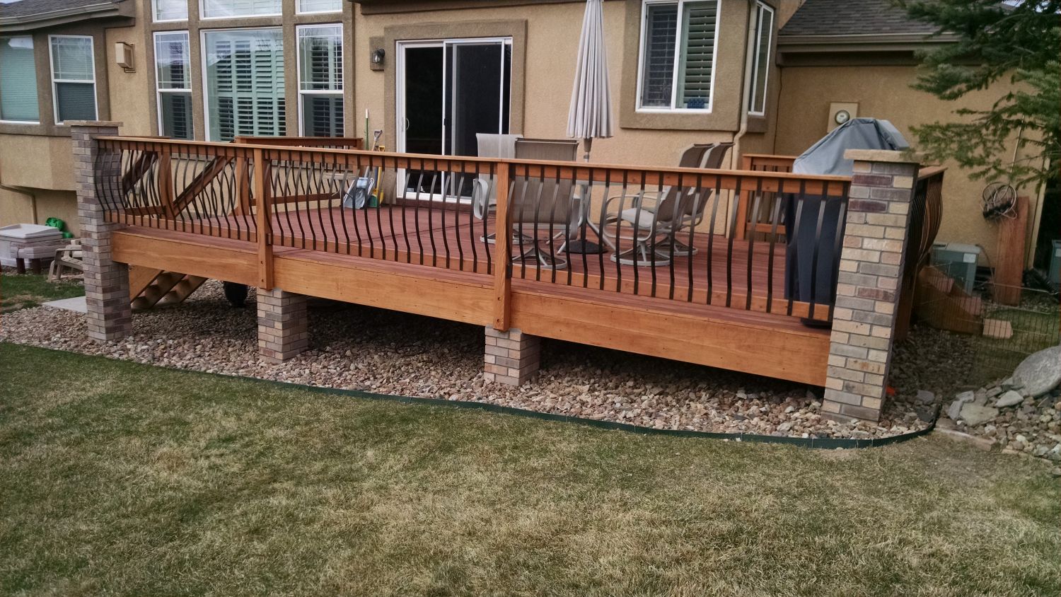 Redwood components railing with black metal Vienna-style balusters, anchored by stone columns.