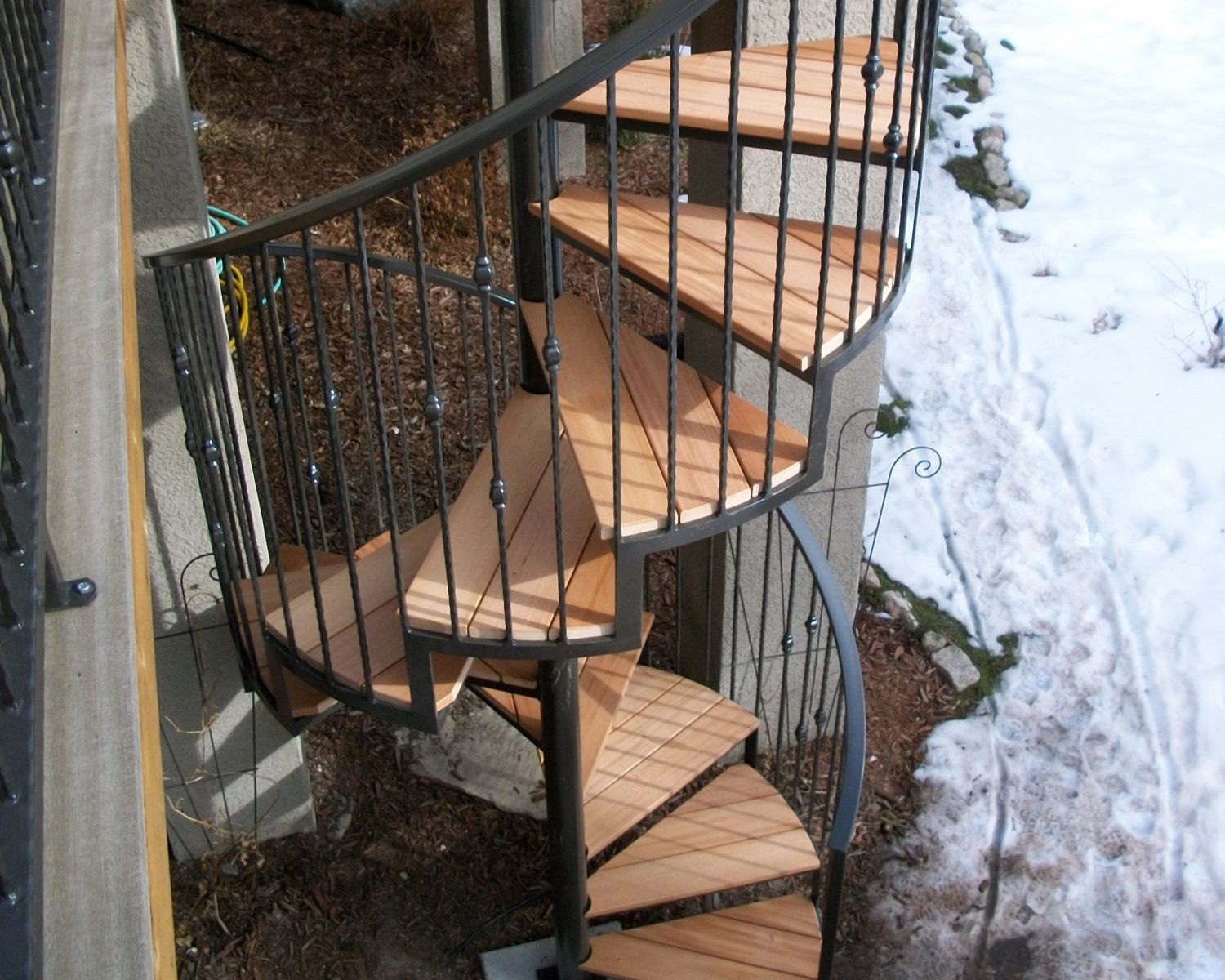 Spiral staircase off a hardwood deck that features a custom-built wrought iron railing.