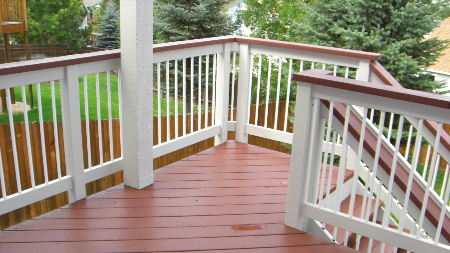 Wood deck railing with white, round, metal balusters and a wood drink cap.
