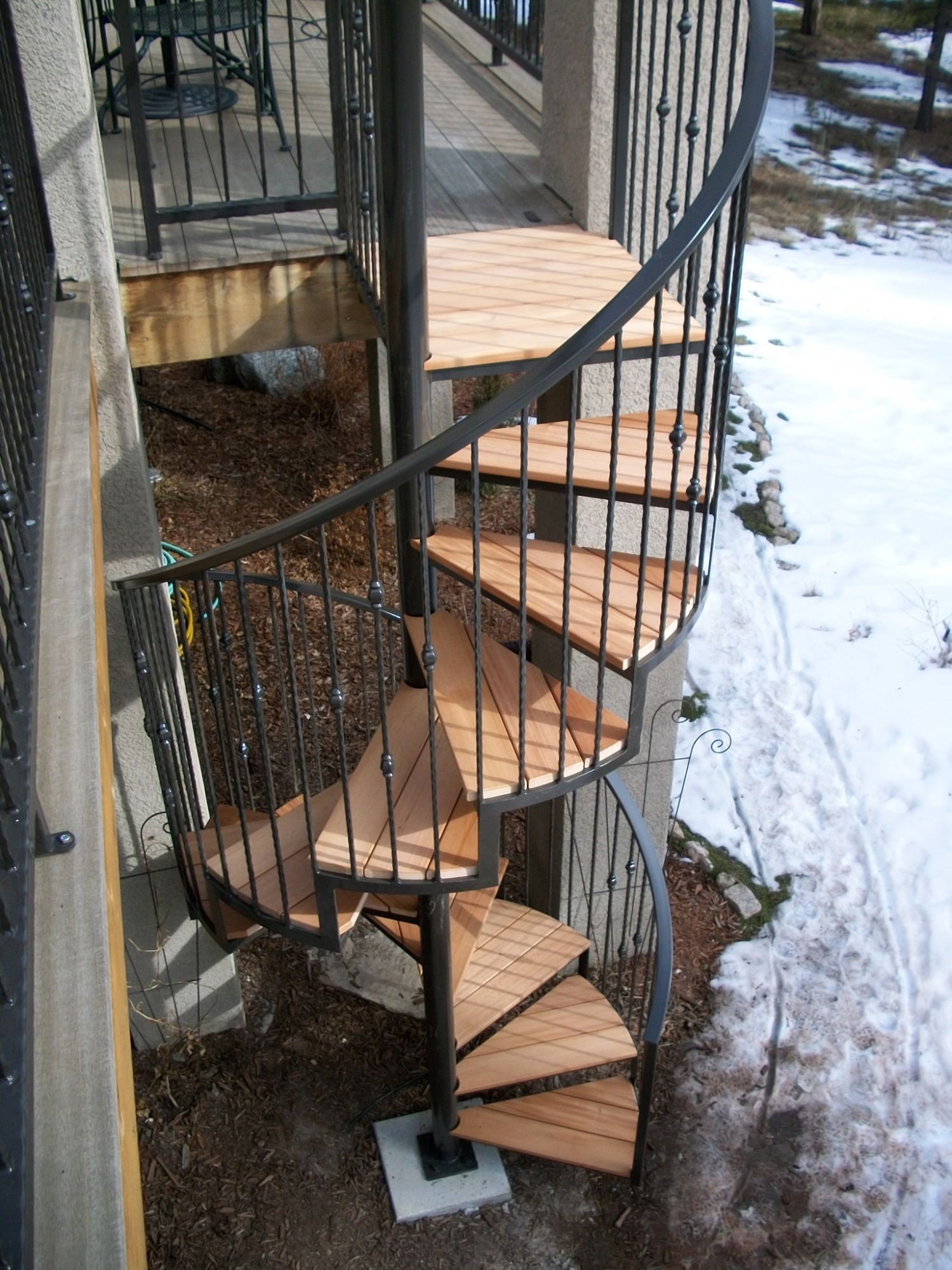 Wrought iron spiral staircase for a deck with hardwood step treads.