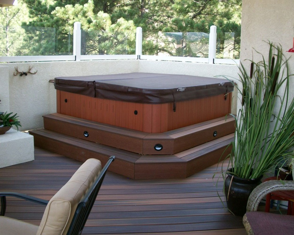 Composite deck with a hot tub in one corner. A stucco-wall features short glass panes on top to act as a windbreak.