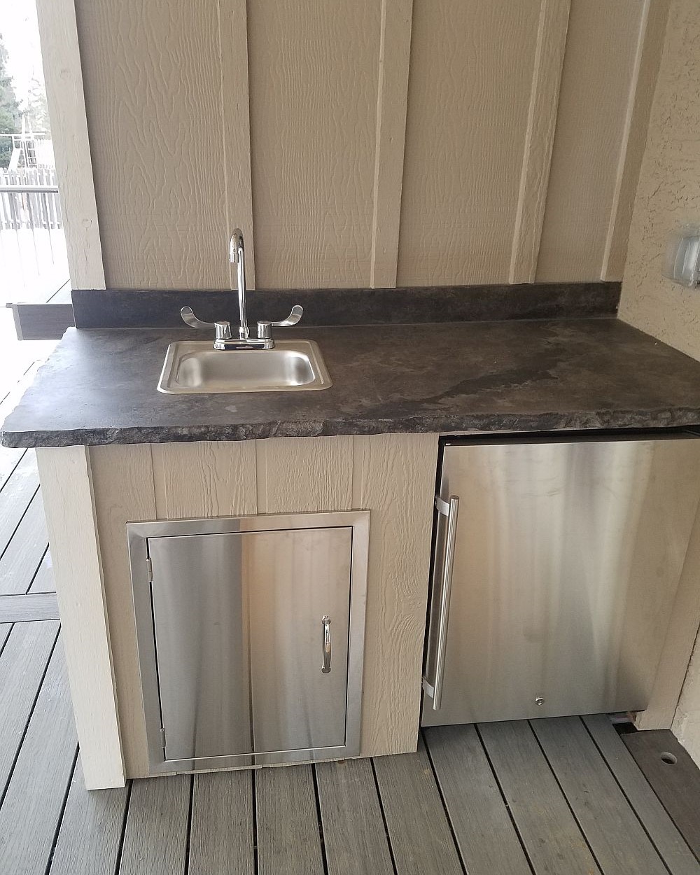 Full-use sink and mini refrigerator are installed on a composite deck to create an outdoor kitchen.