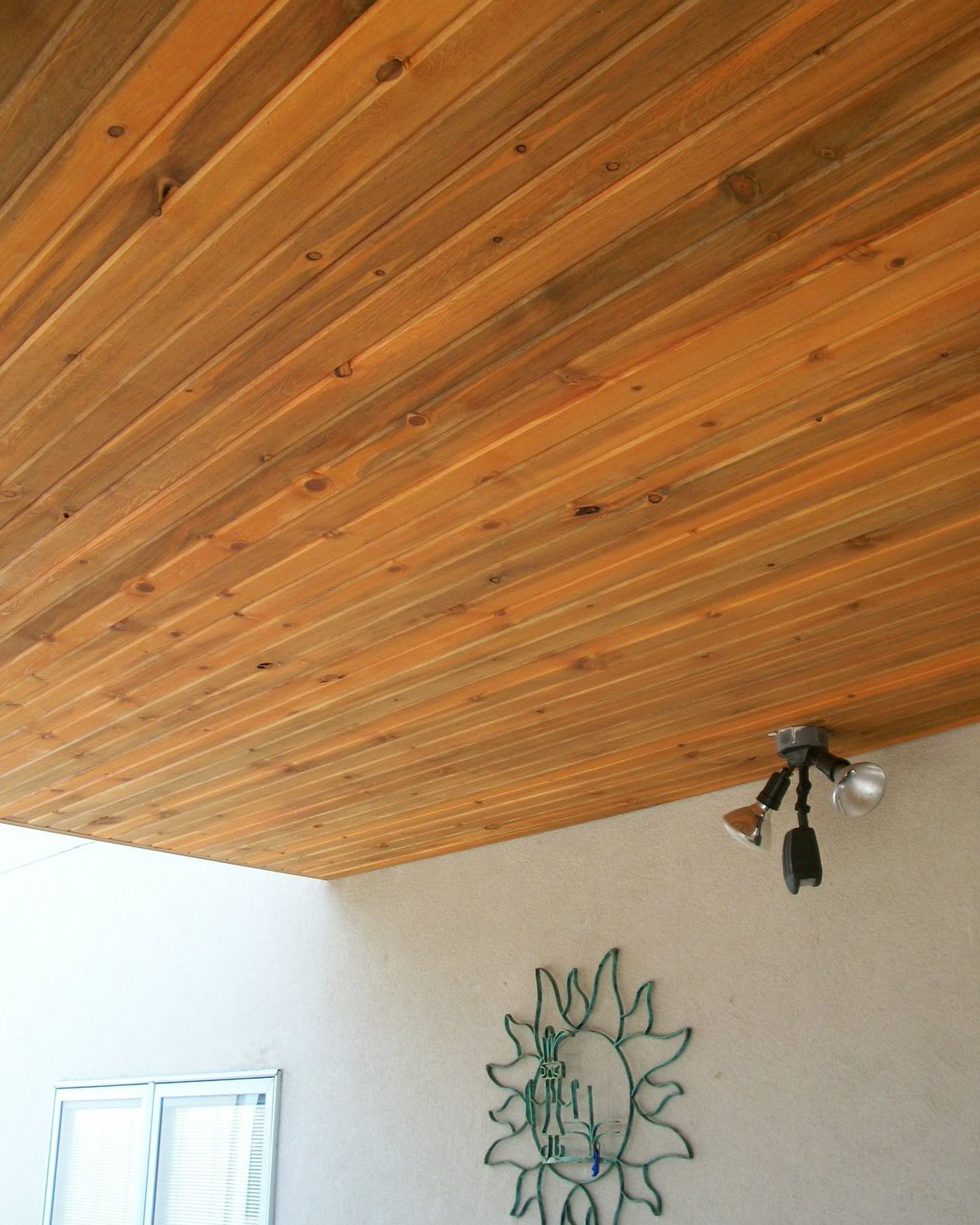 An under-deck drainage system that features a Beetle Kill Pine tongue and groove ceiling with outdoor lighting installed.