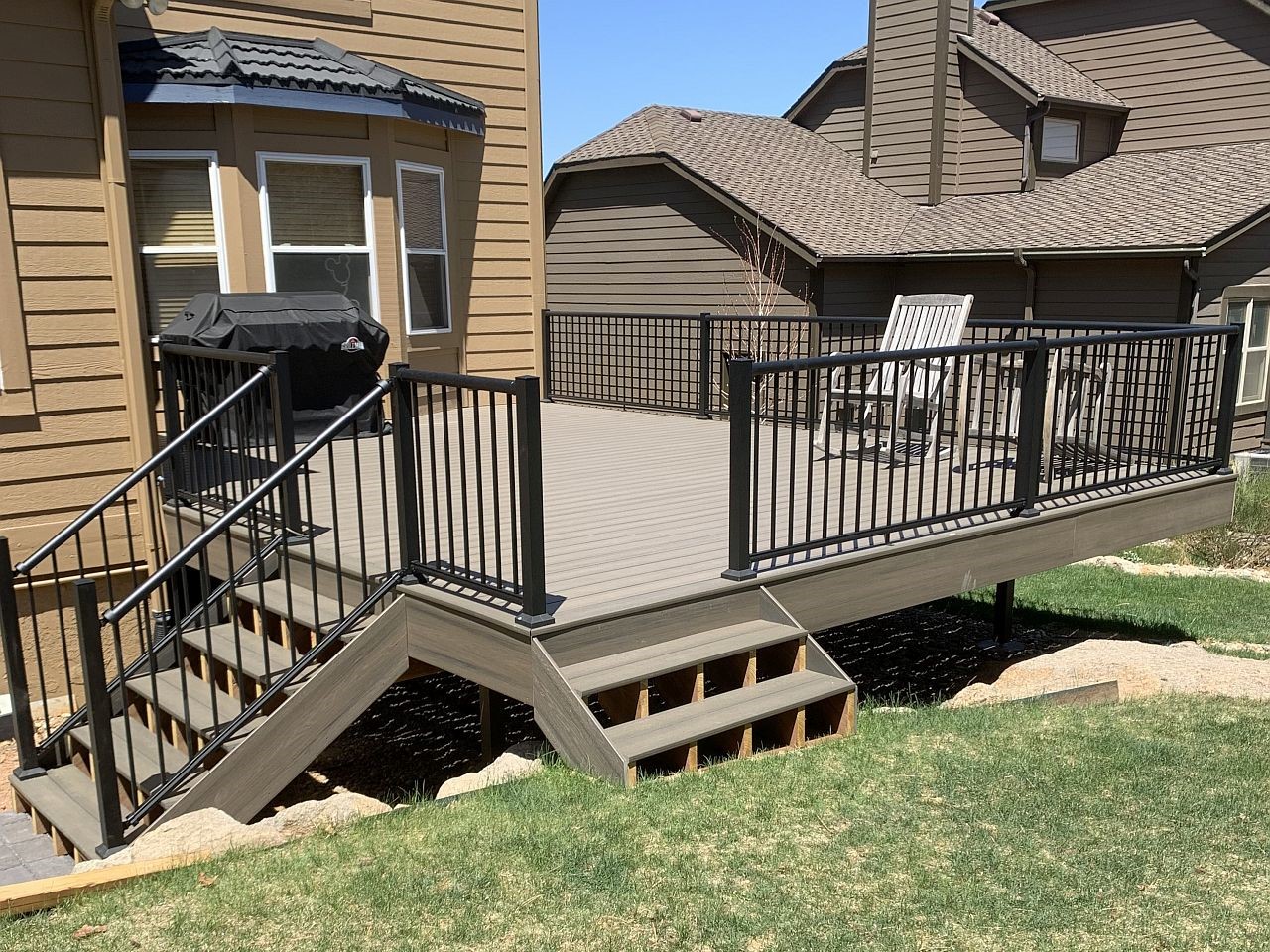 Composite deck with gray decking and a metal panel railing in a matte black. There are two sets of stairs for access to the yard.