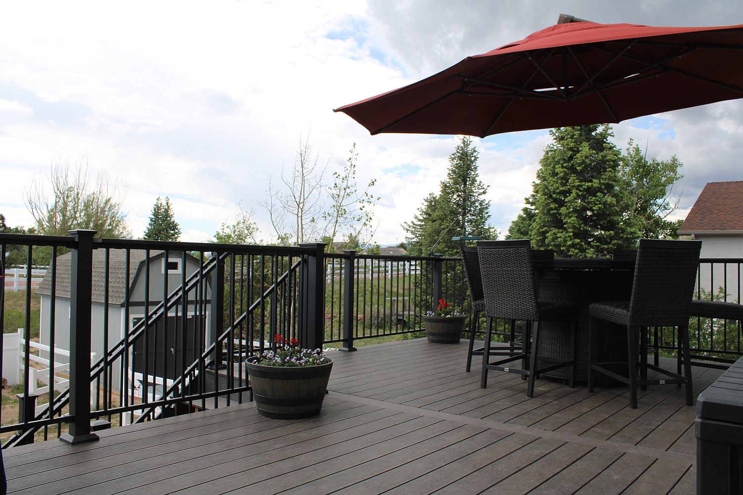 Dark brown composite deck with a matte black railing. A dining set with umbrella is on the right side.