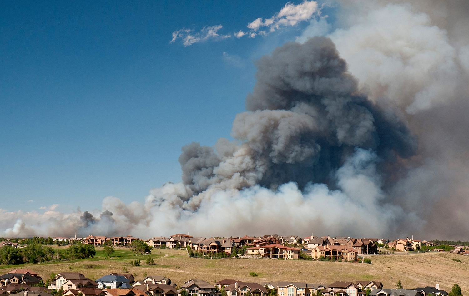 Black clouds from a wildfire hover over a housing development