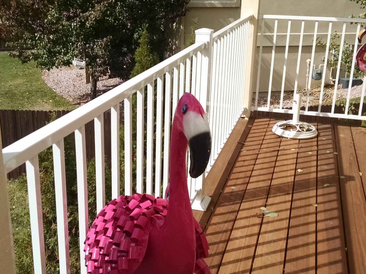 Redwood deck with a white, aluminum deck railing. There is a plastic flamingo ornament in the foreground.