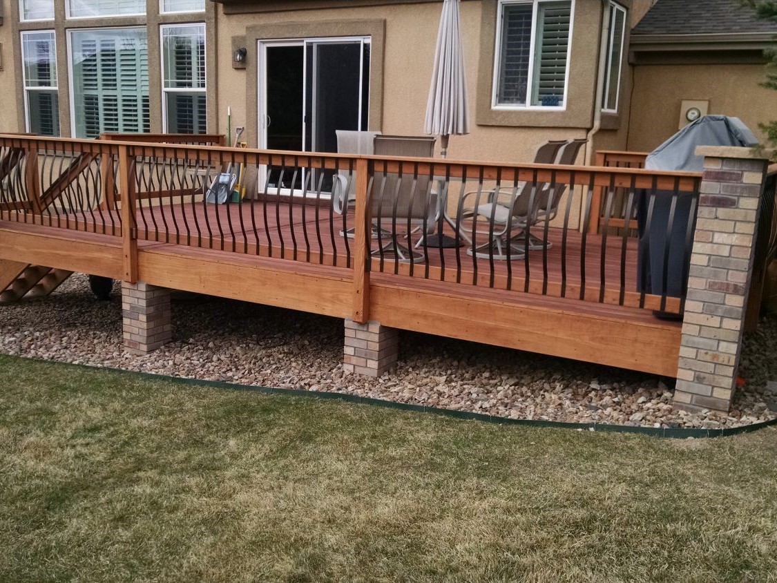 Wood deck railing with matte black Vienna Bow metal balkusters and stone columns.