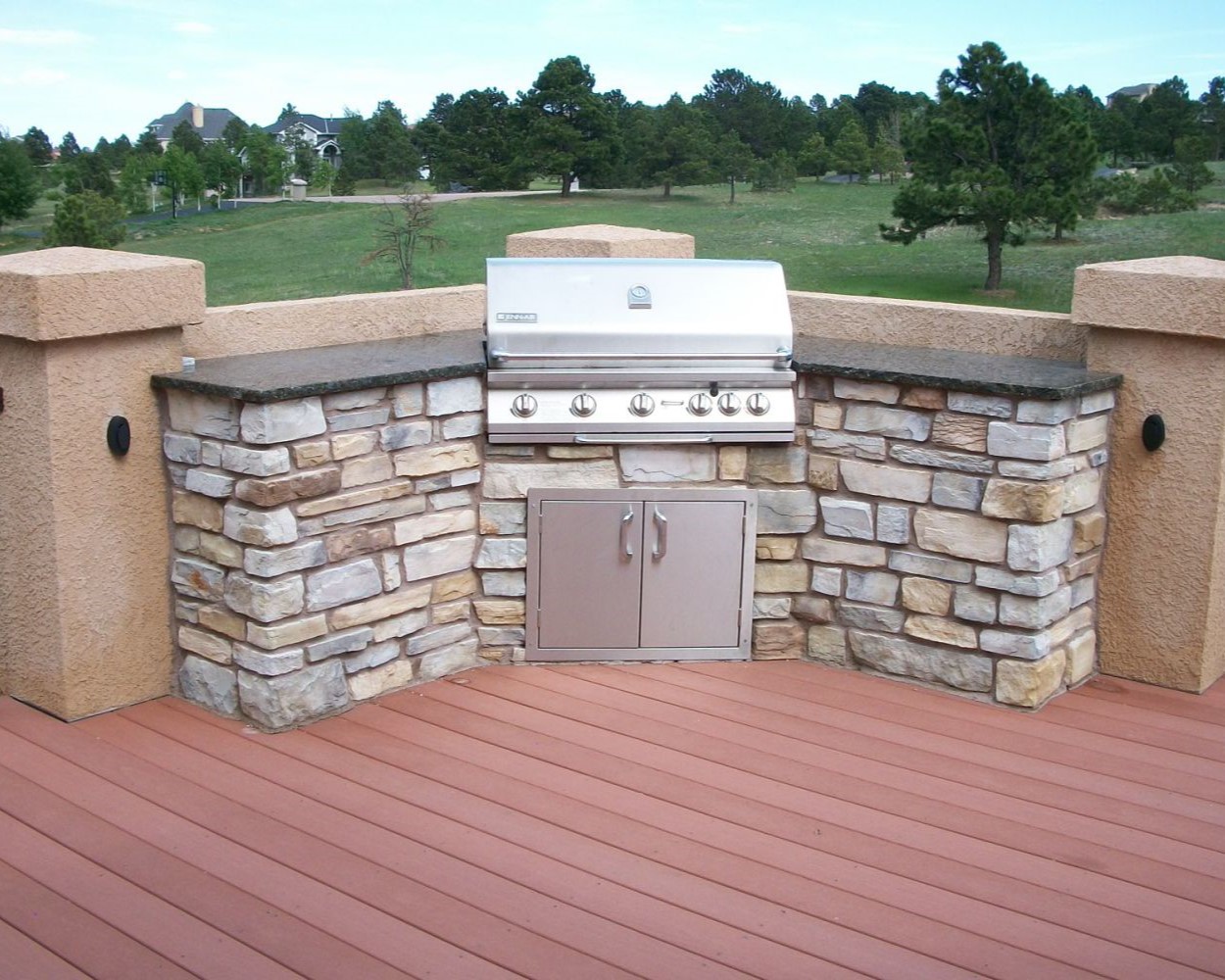 A redwood deck that features a corner with stucco columns and a built-in grill area. The grill area has a rock base and granite countertops